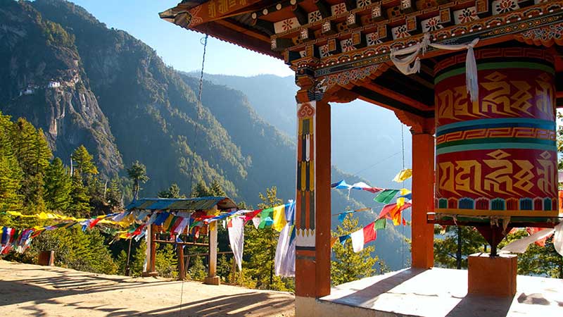 1533987295 view of the taktshang monastery in paro bhutan with prayer flags and a prayer wheel in the front